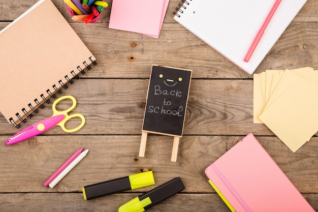 Wooden plaque with the inscription Back to school near notepads scissors and other stationery on brown wooden table