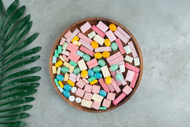 Wooden plate of colorful chewing gums on stone surface.