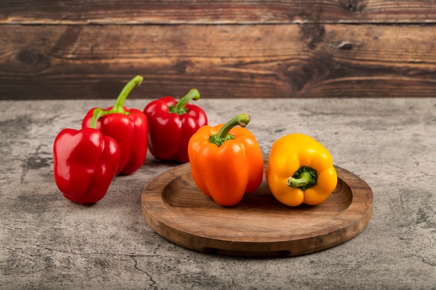 Wooden plate of colorful sweet bell peppers on stone surface