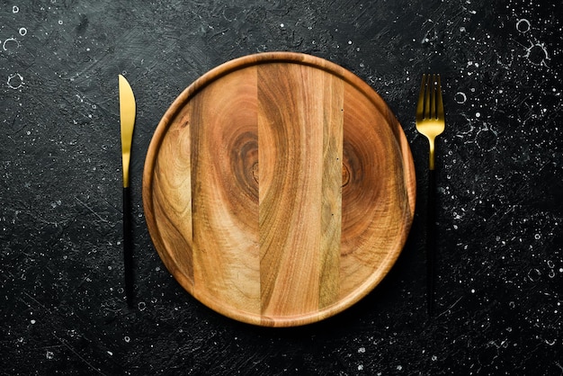 Photo wooden plate and cutlery table setting top view on a stone dark background