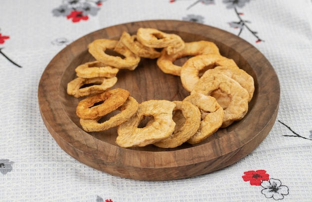 Wooden plate of dried apple rings on white tablecloth.
