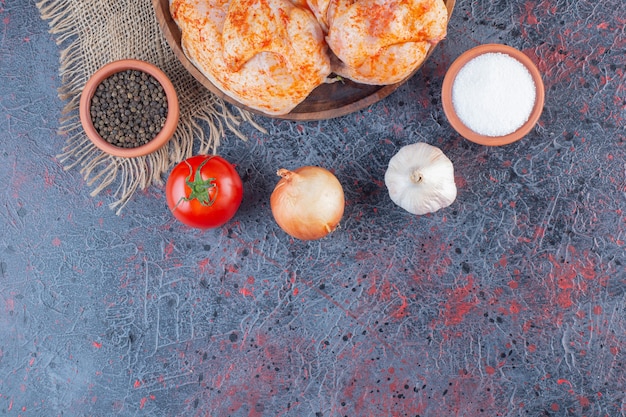 Wooden plate of marinated whole chicken on marble surface.