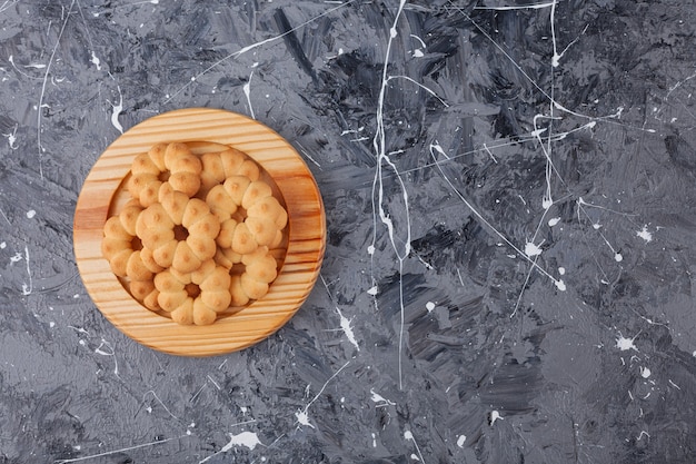 Деревянная тарелка сладкого печенья в форме цветка на мраморном фоне.