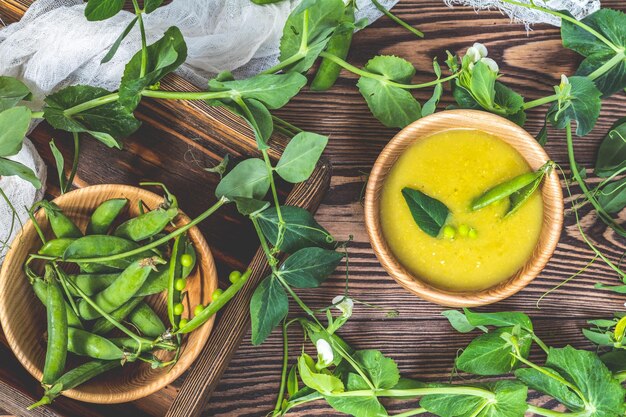 Wooden plate of pea soup and pods of fresh green peas on a dark wooden surface Vintage wooden surface for design with beautifully located pods of green peas Shallow depth of field