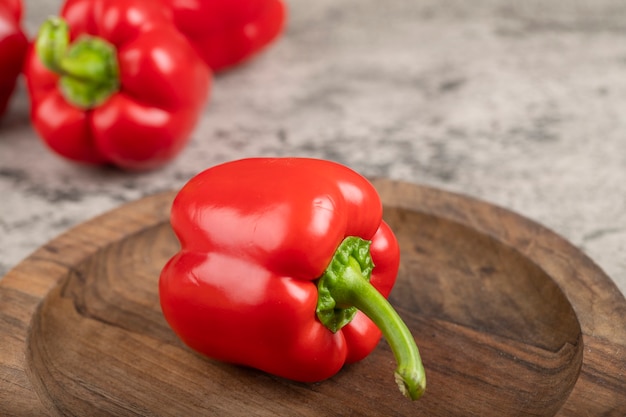 Wooden plate of ripe red bell peppers on stone surface