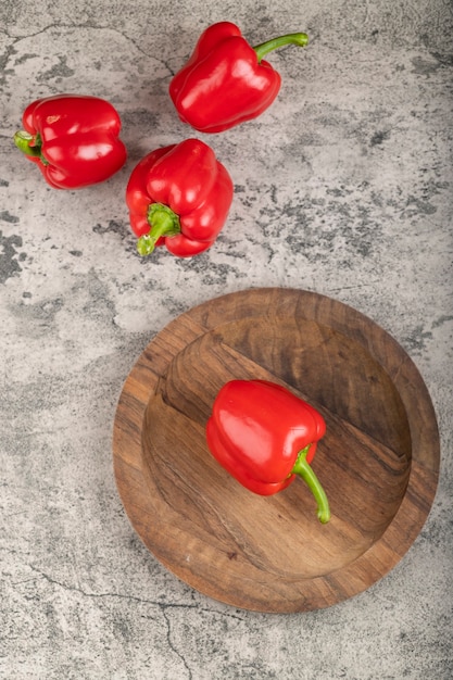 Wooden plate of ripe red bell peppers on stone surface