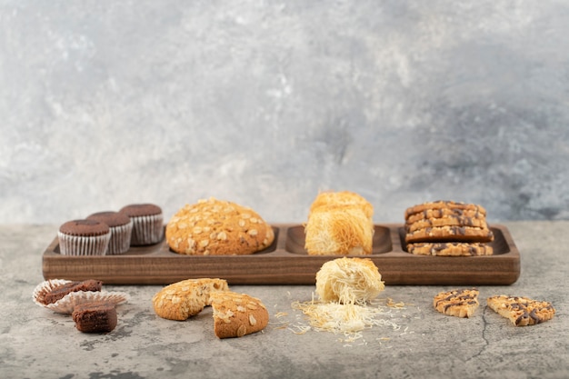 Wooden plate of various sweet desserts placed on stone.