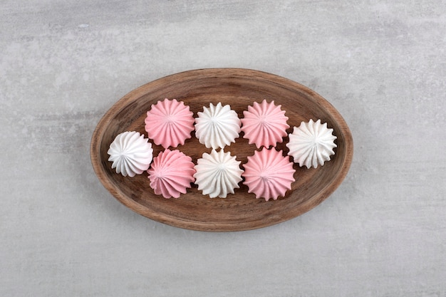 Wooden plate of white and pink meringue dessert on stone surface.