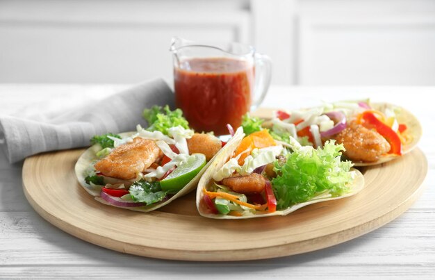Wooden plate with delicious fish tacos on table