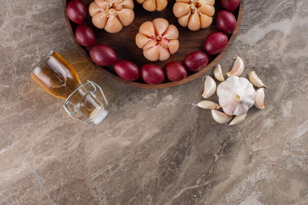 Wooden plate with fermented fruits and garlic on stone table.