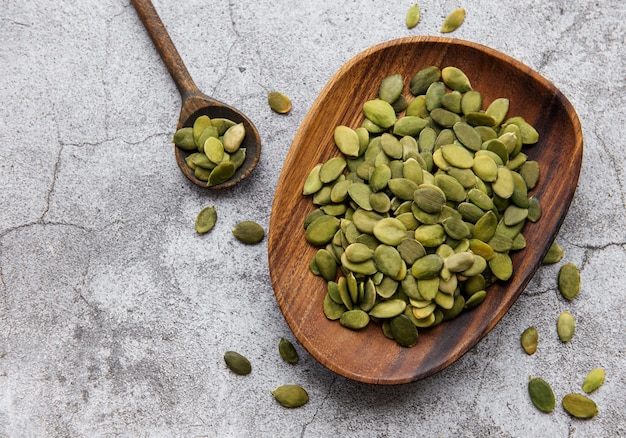 Wooden plate with pumpkin seeds on a gray concrete background