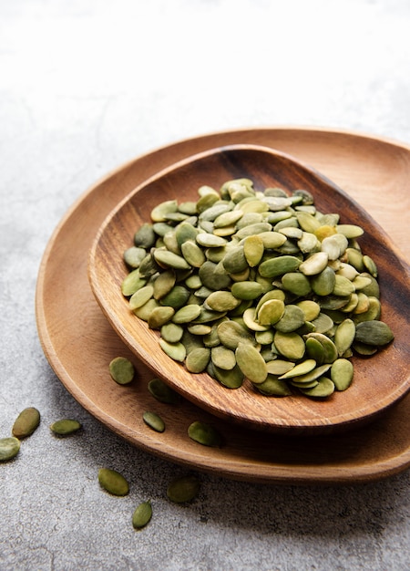 Wooden plate with pumpkin seeds on a gray concrete surface