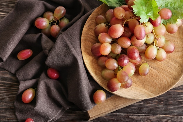 Wooden plate with ripe grapes on table