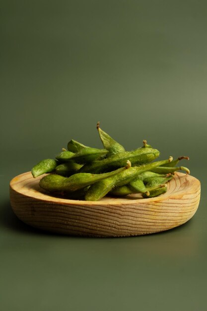 Wooden plate with soybean pods on green smooth background