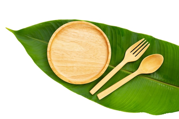 Wooden plate with spoon and fork on green leaves