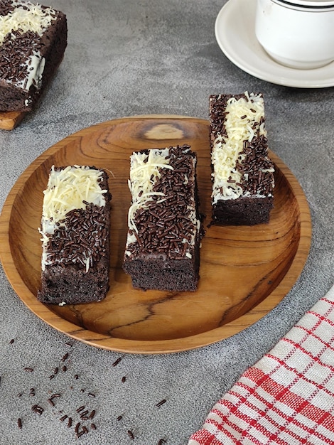 A wooden plate with three pieces of chocolate cake on it and a red and white napkin on the side.