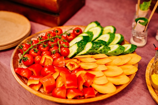 wooden plate with vegetable slicing of tomatoes, cucumbers, sweet peppers and cherry tomatoes.