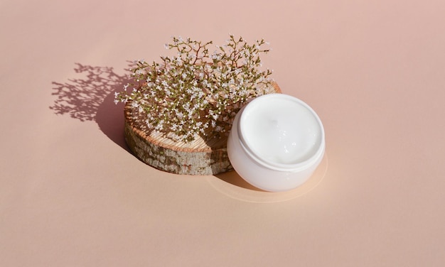 Wooden podium and dry flower with a white jar of cosmetic products