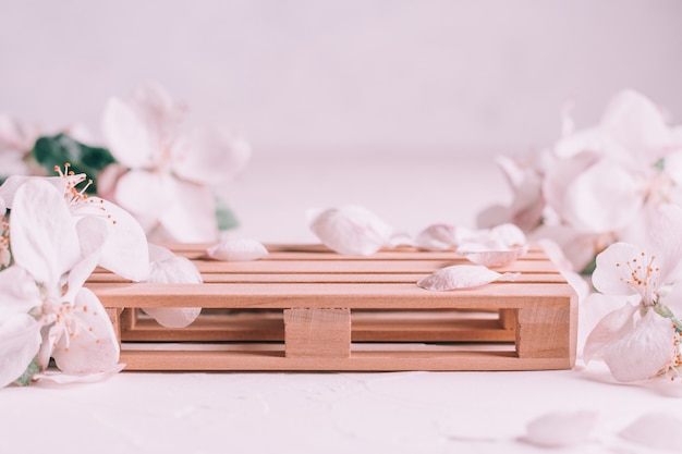 Wooden podium in form of pallet on light plaster surface with apple flowers. Podium, pedestal or stage. Mockup for cosmetic products