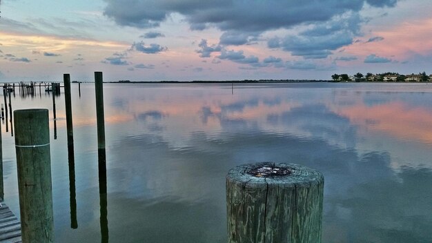 Wooden poles at sea against sky during sunset