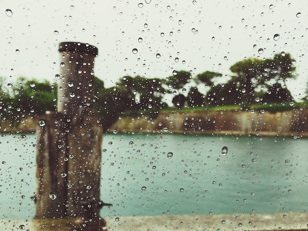 Photo wooden post in river against sky seen through wet glass window during monsoon