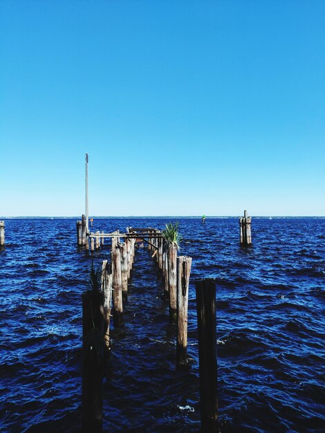 Wooden posts in sea against clear sky