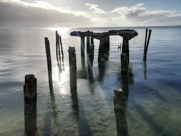 Wooden posts in sea against sky