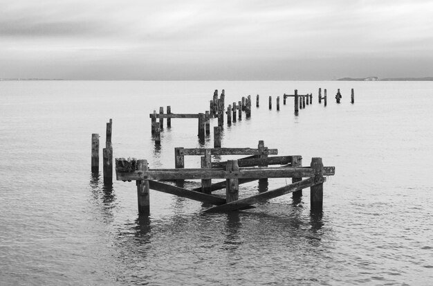 Wooden posts in sea against sky