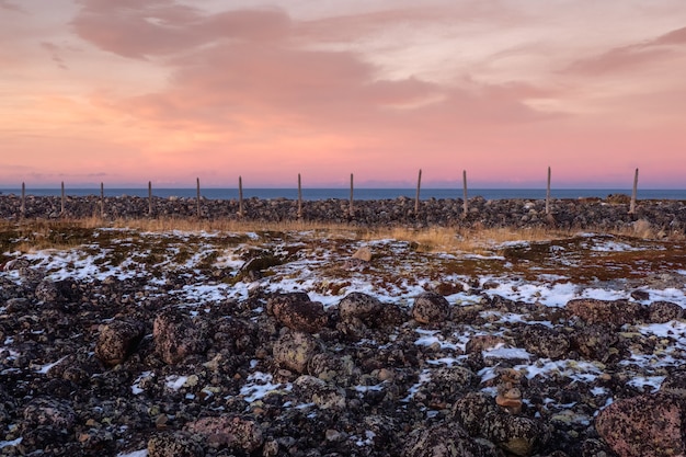 Wooden posts of the snow barrier. Mountain evening landscape with tundra on the Barents sea.