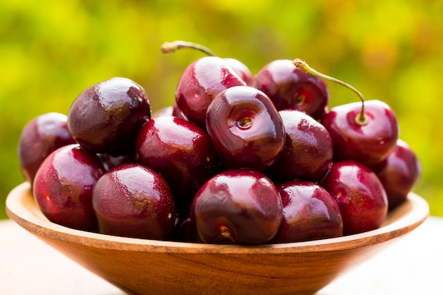 A wooden pot full of cherries over a wooden surface. Fresh fruits