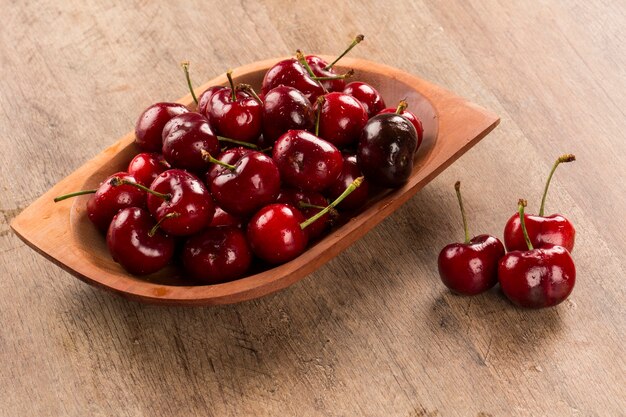 A wooden pot full of cherries over a wooden surface. Fresh fruits