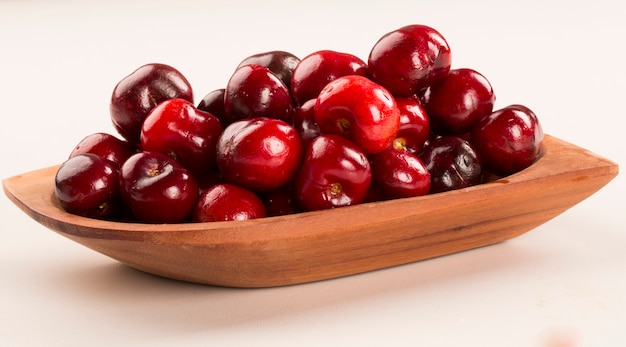 A wooden pot full of cherries over a wooden surface. Fresh fruits