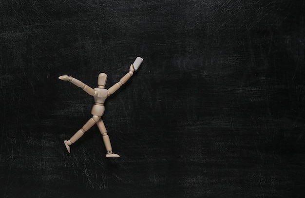 Photo wooden puppet holding chalk on a blackboard