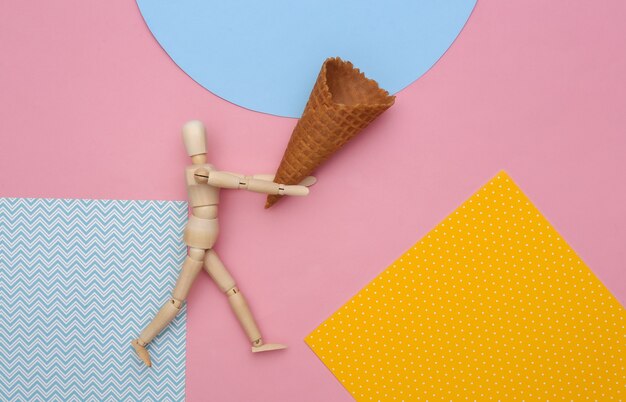 Wooden puppet holding Ice cream waffle cone on colored background. 