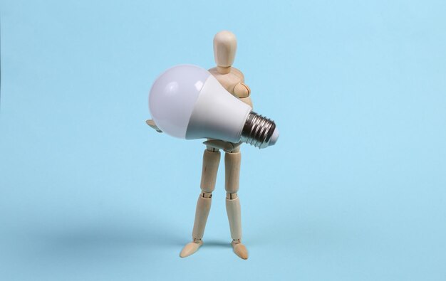 Wooden puppet holding led light bulb on a blue background.