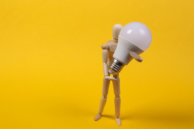 Wooden puppet holding led light bulb on yellow background.