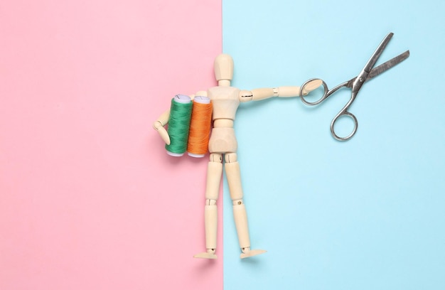 Wooden puppet holding Skeins of colored thread and scissors on a bluepink pastel background Hobbie