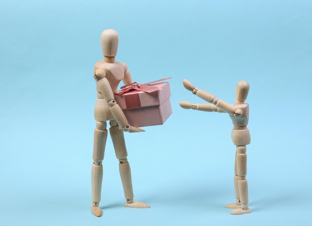 Wooden puppet presents gift box to child on blue background