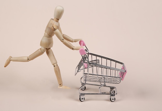 Wooden puppet rolls supermarket trolley on beige background Shopping concept
