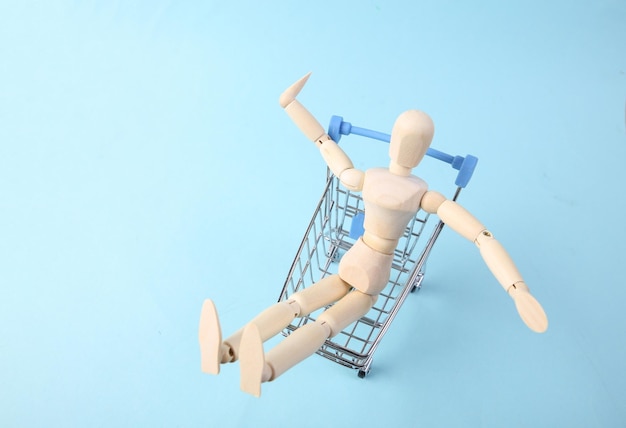 Wooden puppet in a shopping cart on blue background