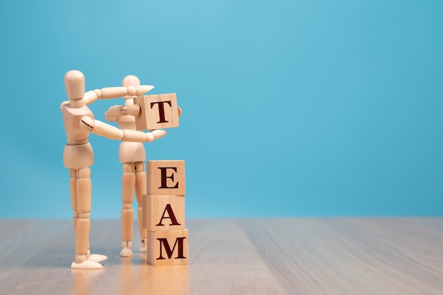 Wooden puppet standing and holding a wooden cube for making a team word.