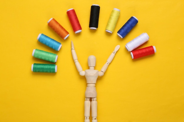 Wooden puppet with Skeins of colored thread on yellow pastel background