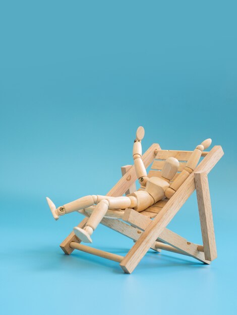 Wooden puppet on the wooden beach chair on blue screen background.