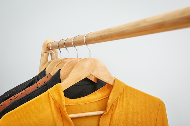 Wooden rack with stylish clothes on light background closeup