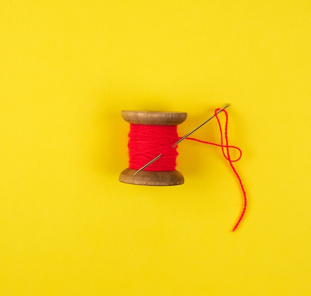 Wooden reel with red wool thread and a large needle