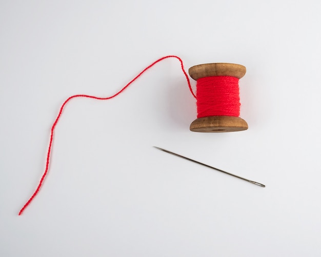Photo wooden reel with red wool thread and a large needle