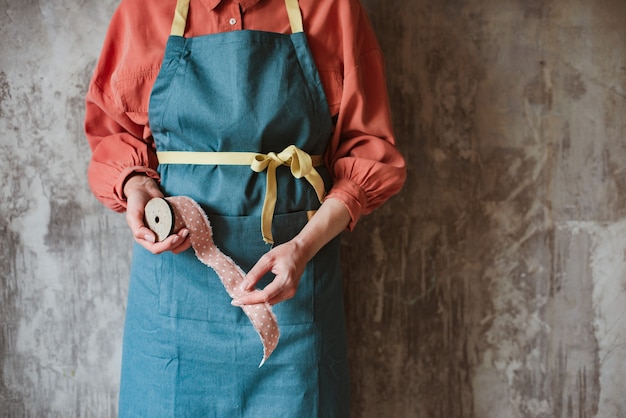 Wooden retro reel with pink polka dot braid in the female hands of a needlewoman in an apron