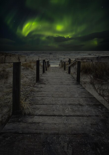 A wooden road among the dunes leading to against the background of the Aurora Borealis