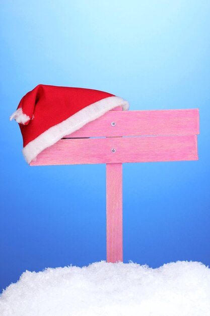 Wooden road sign with Santa hat on blue background