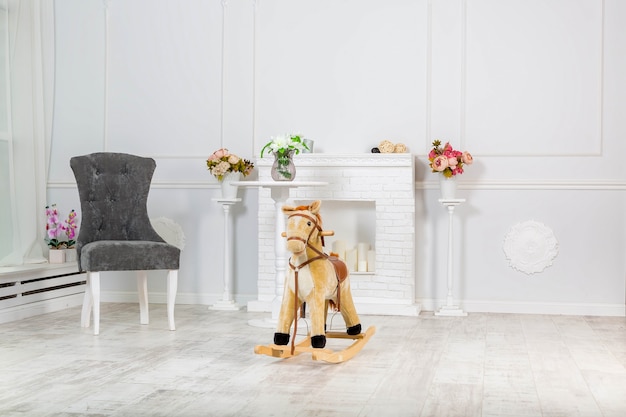 木製のロッキングホースのおもちゃは、装飾的な暖炉とその近くの薄壁の灰色の椅子の近くに立っています